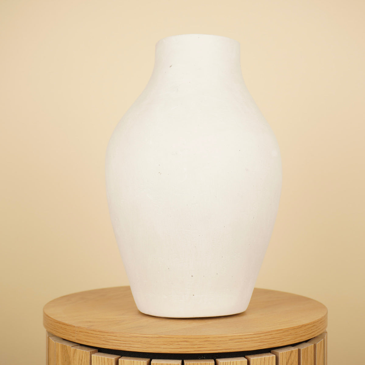 Crèmekleurige vaas met ronde buik, smalle hals en matte afwerking op een houten tafel.